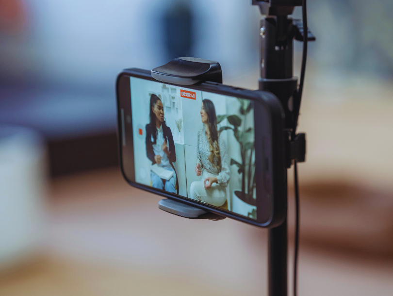 Zwei Frauen führen ein Interview, das mit einem Smartphone auf einem Stativ gefilmt wird – Fokus auf Bildschirmaufnahme.