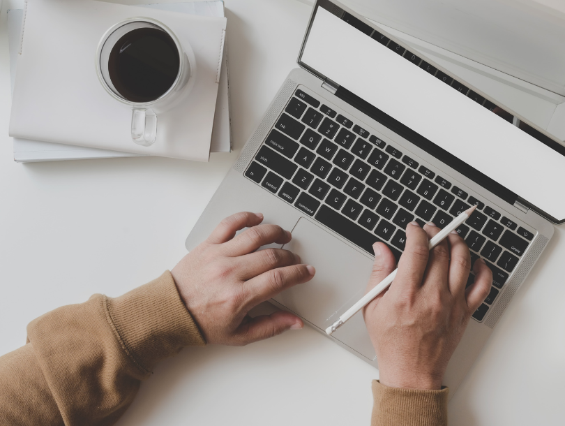 Laptop und Tasse auf weißen tisch. Mensch typt auf laptop mit Touchstift in der Hand