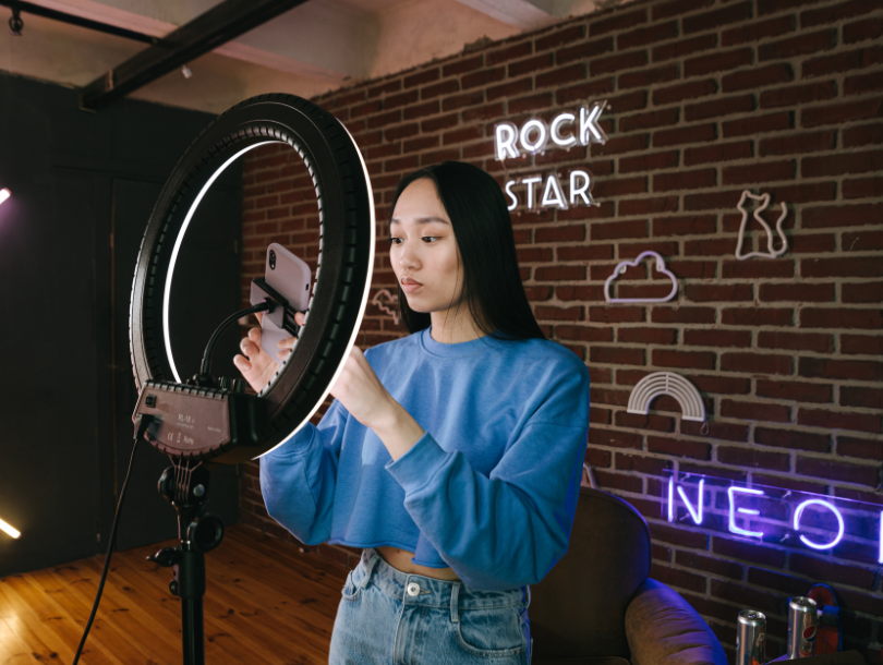 Influencer hinter Lichtring mit Handy und Neonlichter an der Wand