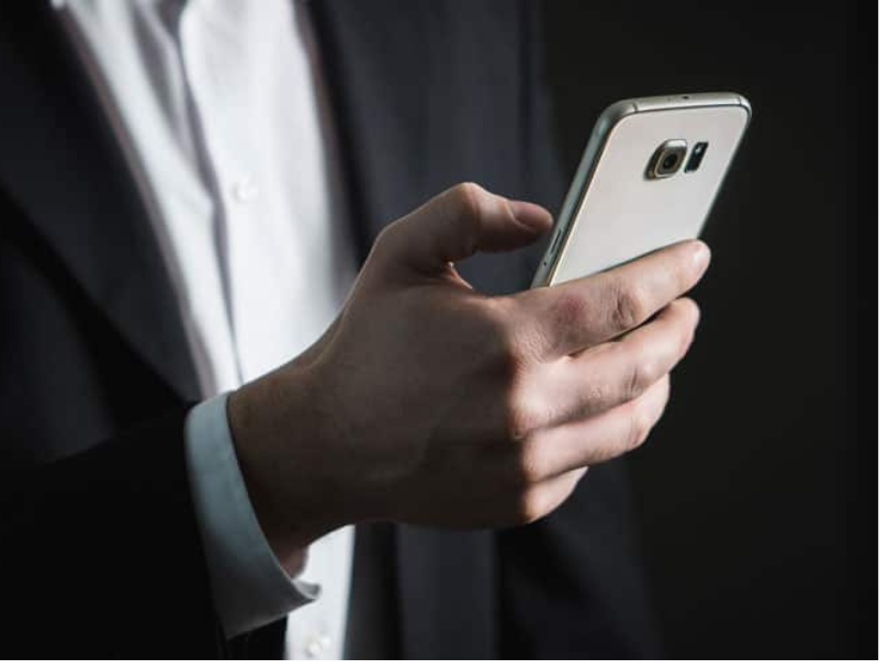 Mensch in Anzug mit Handy in der Hand.