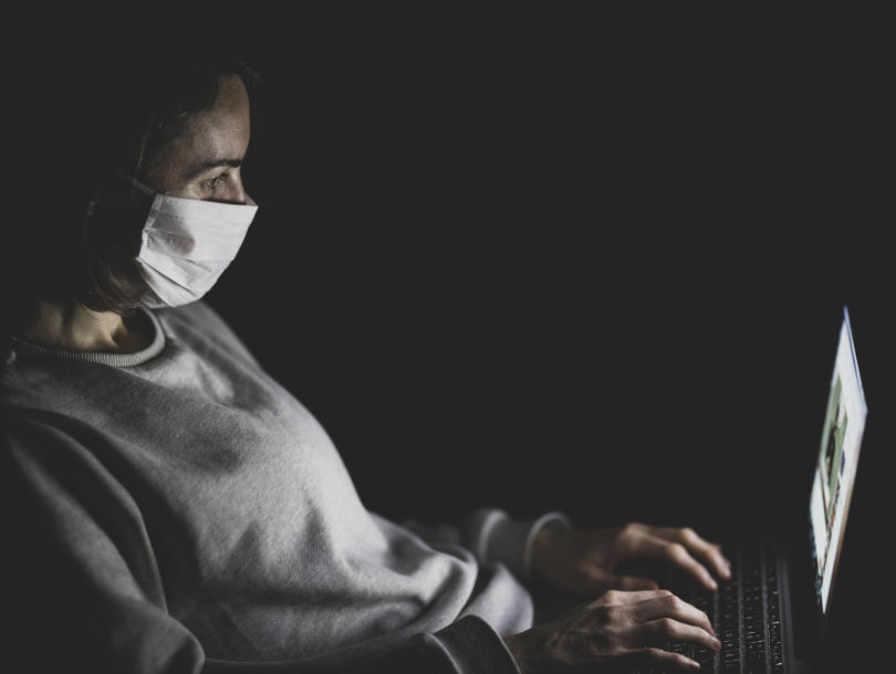 Person hinter Lapto mit Maske über den Mund.