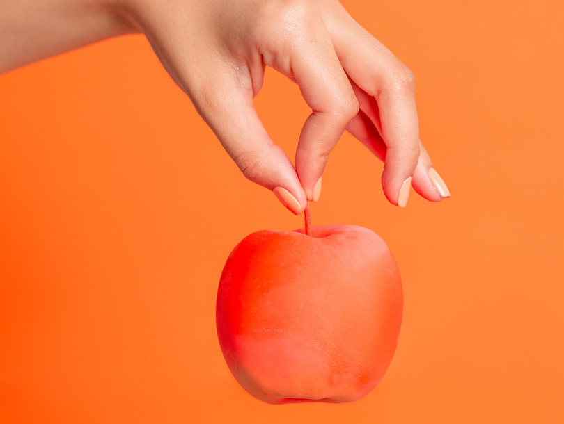 Menschliche Hand, die einen roten Apfel am Stiel hält
